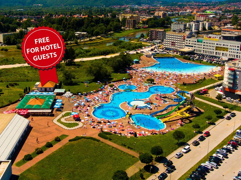 Hotel Hills Sarajevo Congress & Thermal Spa Resort Ilidža Exteriér fotografie The photo shows an aerial view of a large swimming pool area, likely part of a hotel or resort. There are several pools of different shapes and sizes, including one that resembles a Mickey Mouse shape. The area is filled with numerous sun loungers an